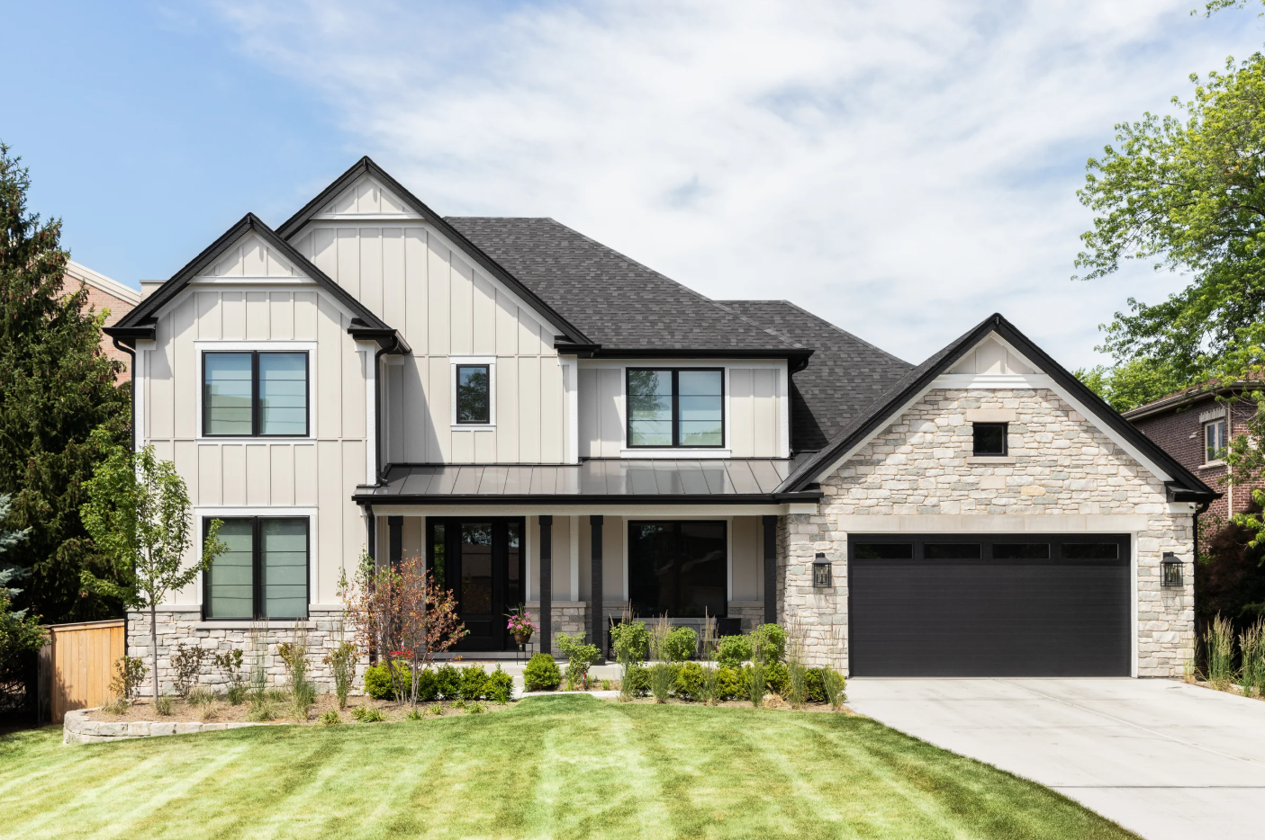 Oak Park, IL, USA - May 30, 2022: A tan modern farmhouse with a wainscoting siding, covered front porch, beautiful landscaping, and stone covered garage.